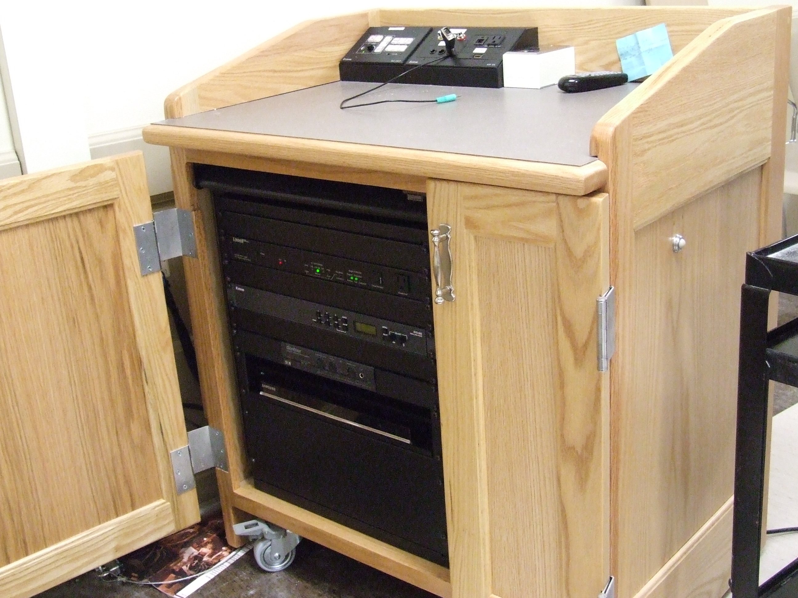 A view of the open cabinet with HDMI input, a push button controller, and audio visual rack.