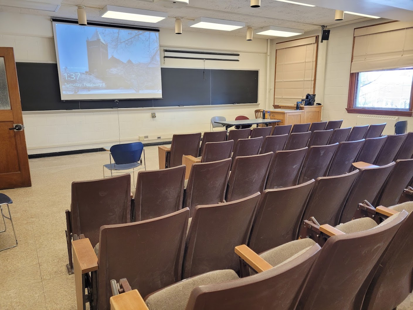 A view of the classroom with theatre auditorium seating, chalkboards, and an instructor table in front.