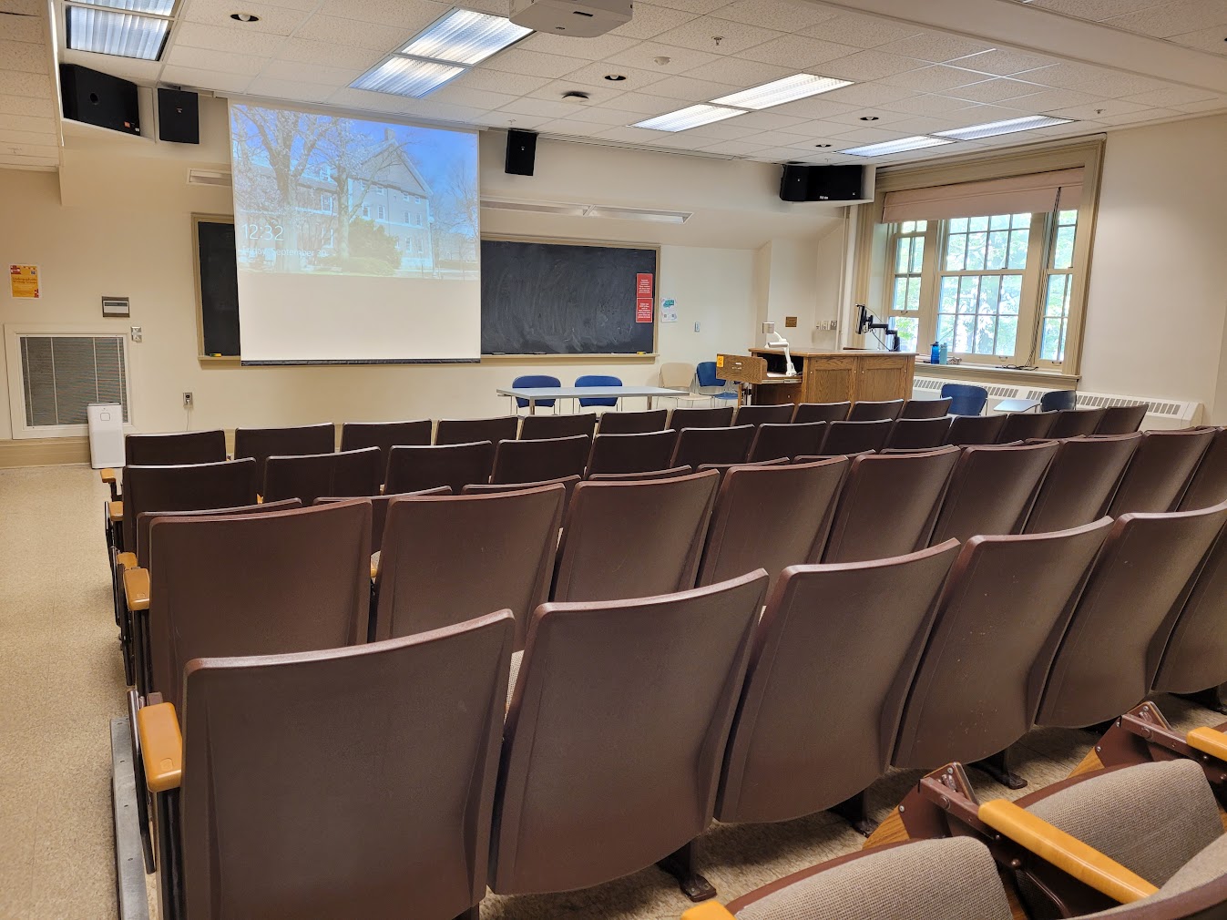 A view of the classroom with theatre seating, chalkboard, and instructor table in front.