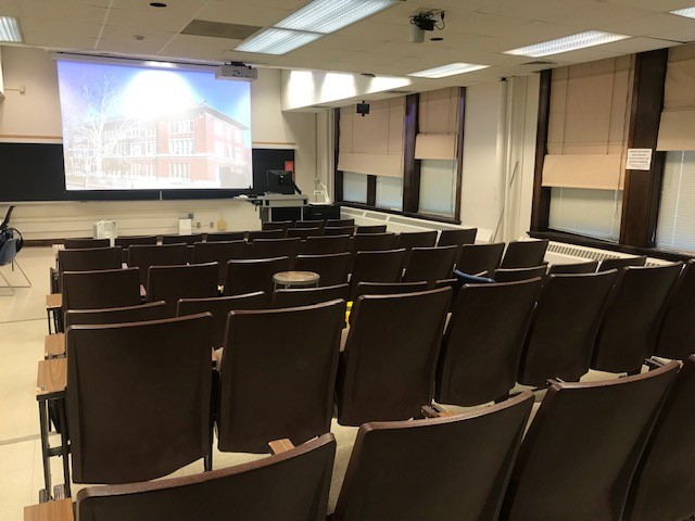 A view of the classroom with theater auditorium seating, chalkboard, and instructor lectern in front.