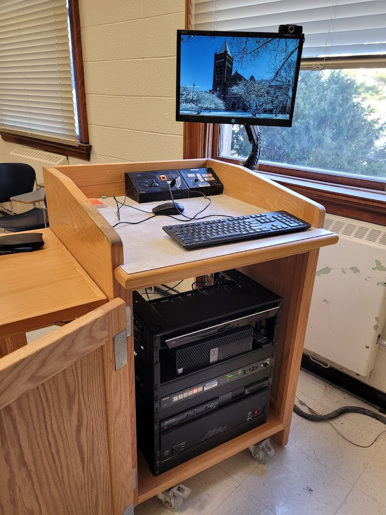 A view of the open cabinet with a computer monitor, VGA and HDMI inputs, a push button controller, and audio visual rack. 