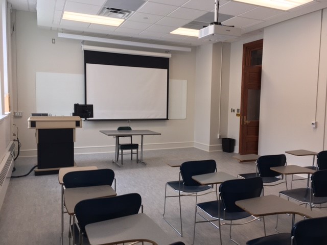 A view of the classroom with movable tableted arm chairs, white board, and instructor table in front.