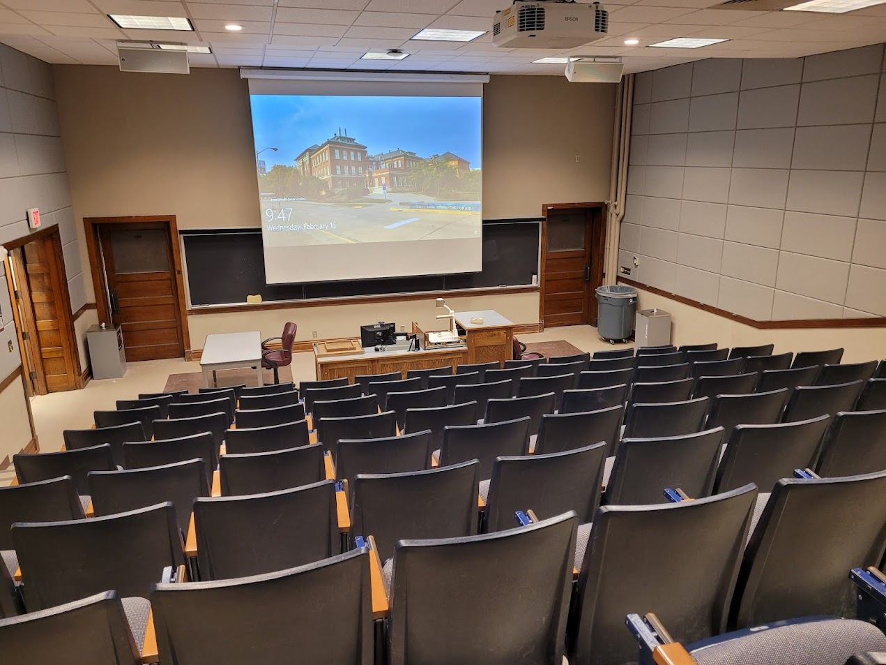 A view of the classroom with theater auditorium seating, chalkboard, and instructor table in front.