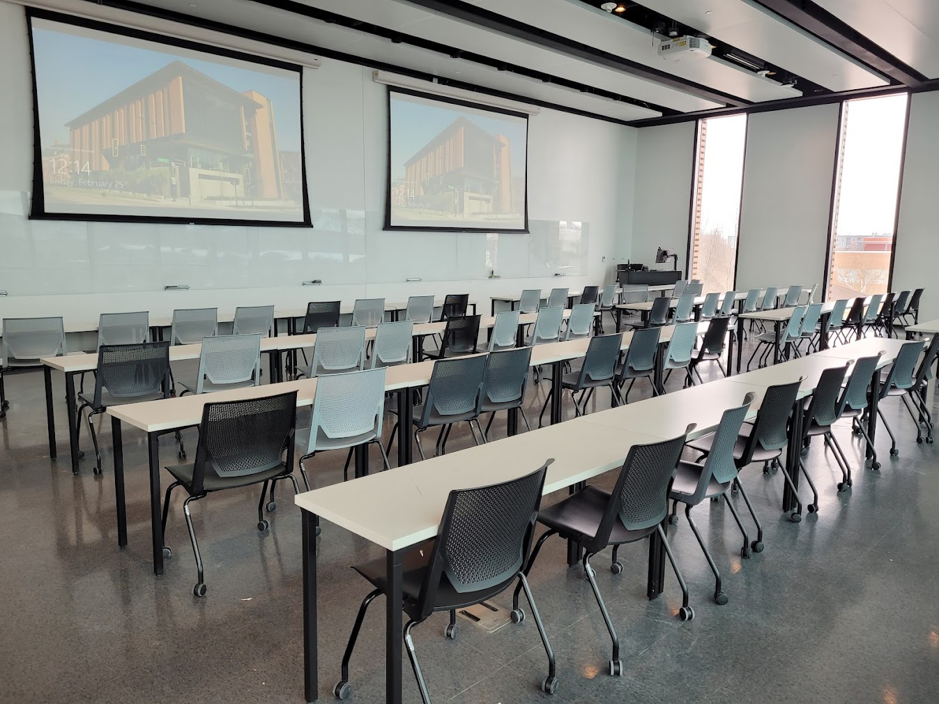 This is a view of the room with student desks, projection screens, a front lecture table, and whiteboards.