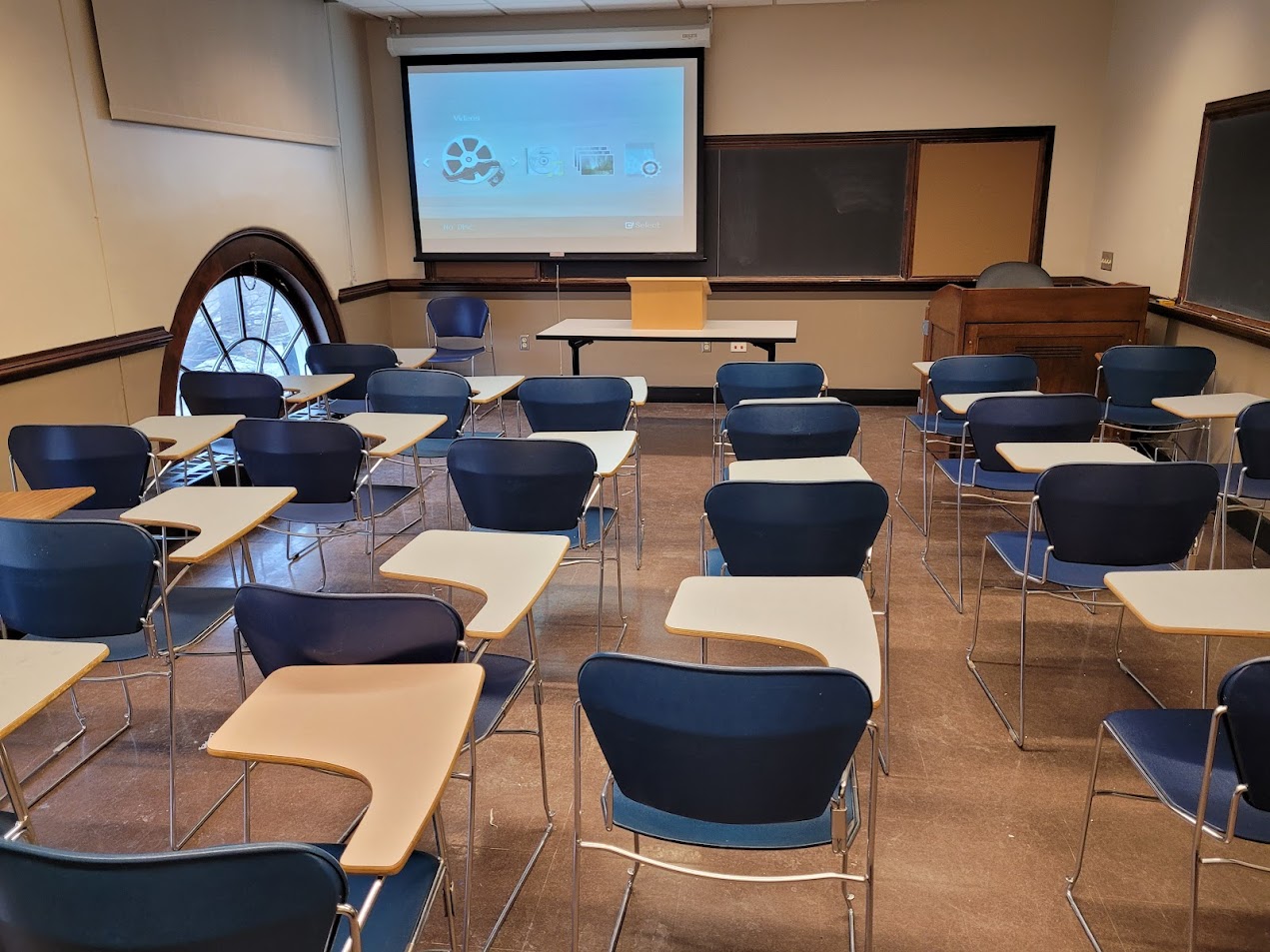 A view of the classroom with movable tableted arm chairs and chalkboard.