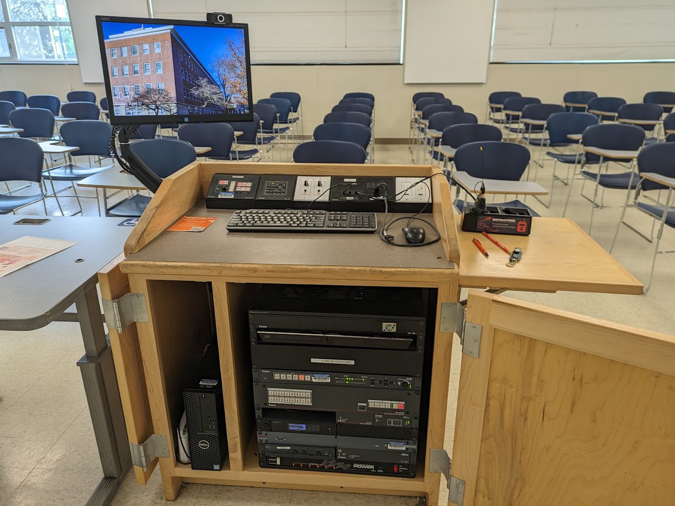 A view of the open cabinet with PC, and HDMI inputs, Blu-ray DVD player, a push button controller, audio visual rack, rechargeable Wireless Microphone,  and electric screen controls.