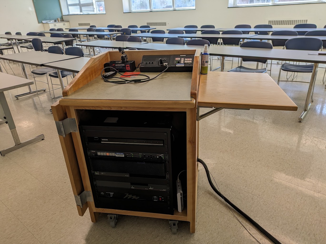 A view of the open cabinet with HDMI input, Rechargeable Wireless Microphone, DVD Player, a push button controller, and audio visual rack.